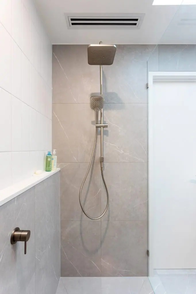 grey shower wall tile with white shelf and shower rail