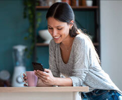 A young woman is sitting at the kitchen counter, browsing her phone while considering home renovation options.